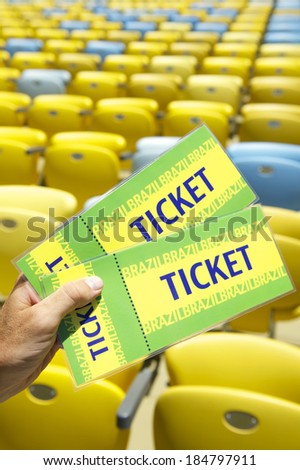 Soccer fan holding two Brazil tickets in front of empty yellow seats