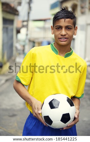 Portrait of smiling young Brazilian football player in holding soccer ball on neighborhood street