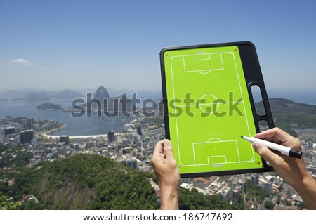 Hands holding soccer football tactics board and pen above bright sunny skyline overlook of Rio de Janeiro Brazil
