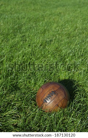 Vintage brown football soccer ball sits in bright sunny green grass field