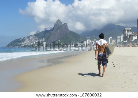 Brazilian surfer walking with surfboard toward Two Brothers Mountain on Ipanema Beach Rio de Janeiro Brazil