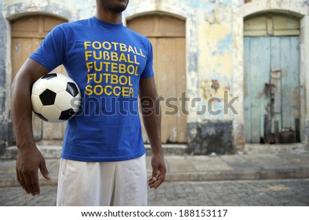 Brazilian soccer player wears blue international football t-shirt holding ball on rustic village street in Nordeste Brazil