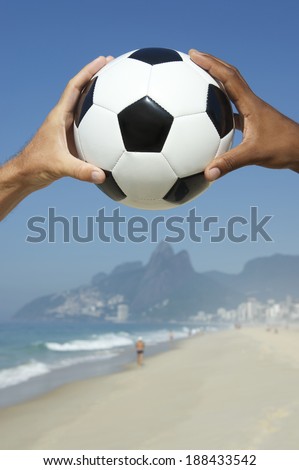 Brazilian interracial hands holding football above Two Brothers Mountain Dois Irmaos Ipanema Beach Rio de Janeiro Brazil