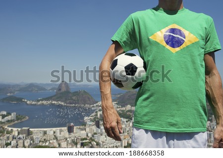 Brazilian soccer player holding football wearing Brazil flag shirt at bright sunny Rio de Janeiro skyline with Sugarloaf Pao de Acucar Mountain