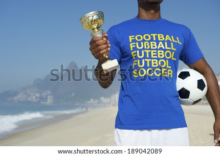 Champion Brazilian football player holding trophy and soccer ball in international football t-shirt Ipanema Beach Rio de Janeiro Brazil
