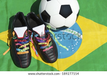 Good luck football boots soccer cleats laced with Brazilian wish ribbons next to ball on Brazilian flag in bright sun