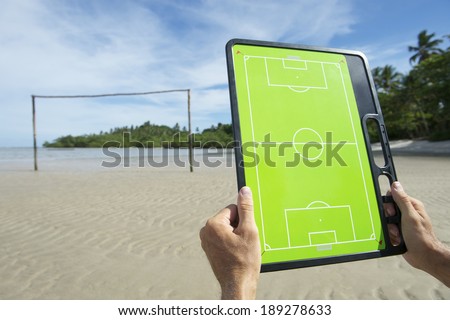 Hands holding soccer football tactics board on rustic Brazil beach football pitch