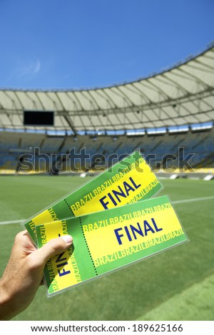 Soccer fan holding two final tickets in front of a bright football pitch in large stadium
