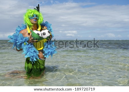 Sexy Brazilian drag queen football fan with green wig and blue boa fondling her soccer balls in the shallow waters of tropical beach