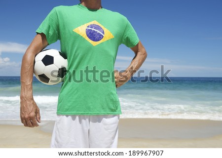 Brazilian soccer player in Brazil flag shirt holding football with hand on hip on tropical Ipanema Beach Rio de Janeiro