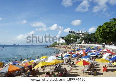 SALVADOR, BRAZIL - MARCH 6, 2014: City residents relax with colorful beach umbrellas on a bright summer afternoon on Porto da Barra beach.