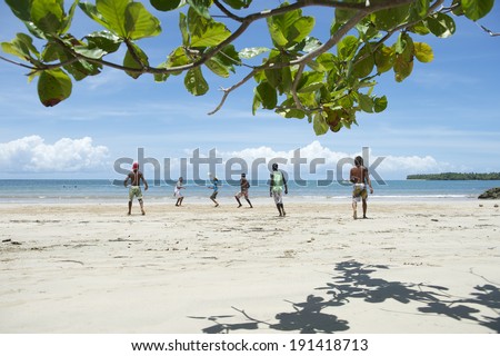 MORERE, BRAZIL - MARCH 8, 2014: Group of young men run on the beach in a midday pelada kickabout football match beyond the shadows of an almond tree.