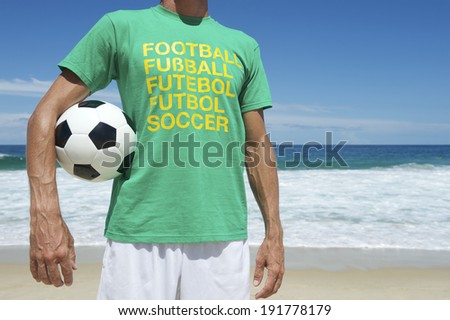 Brazilian soccer player wearing international football shirt holding soccer ball on bright tropical Ipanema Beach Rio de Janeiro