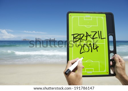 Hands writing Brazil 2014 on football tactics board on empty beach at Ipanema Rio de Janeiro Brazil