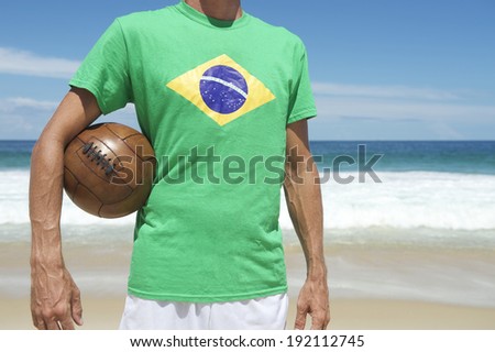Brazilian soccer player in Brazil flag shirt holding vintage football on tropical Ipanema Beach Rio de Janeiro