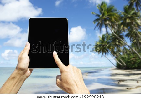 Traveling tourist using touchscreen digital tablet computer at beach in Nordeste Bahia Brazil
