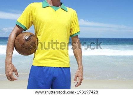 Brazilian soccer player in Brazil colors holding old vintage brown football tropical beach