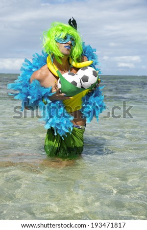 Sexy Brazilian drag queen football fan with green wig and blue boa fondling her soccer balls in the shallow waters of tropical beach