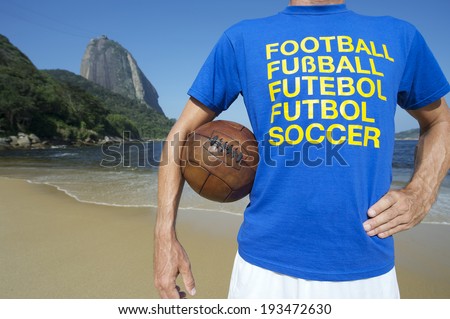 Brazilian soccer player in multi language message t-shirt holding vintage football Red Beach Rio de Janeiro Brazil