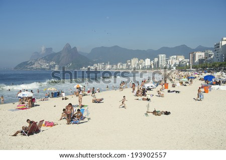 RIO DE JANEIRO, BRAZIL - JANUARY 20, 2014: Residents of Rio relax on Ipanema Beach with the city skyline and Two Brothers Mountain in the background.