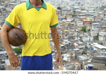 Brazilian football player standing in team Brazil colors kit holding vintage football in front of favela slum background in Rio de Janeiro