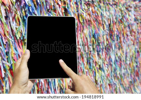 Finger of traveling tourist touching tablet computer at wall of Brazilian wish ribbons at Bonfim Salvador Bahia Brazil