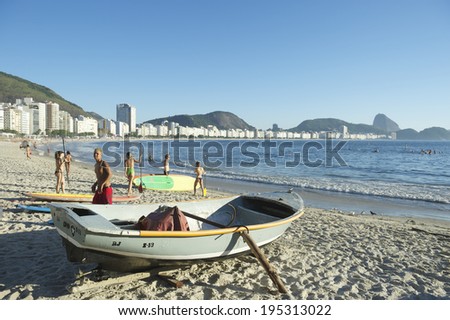 RIO DE JANEIRO, BRAZIL - FEBRUARY 04, 2014: A Brazilian fishing boat sits next to stand up paddlers taking their boards to the sea on a tranquil morning on Copacabana Beach.