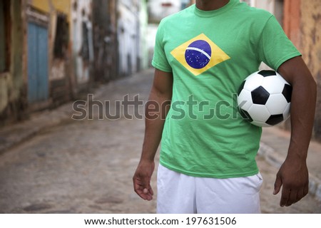 Brazilian street football player standing in Brazil flag t-shirt holding soccer ball in an old rustic village