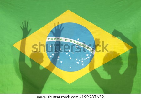 Shadow silhouettes of Brazilians celebrating against Brazil flag in bright sunlight
