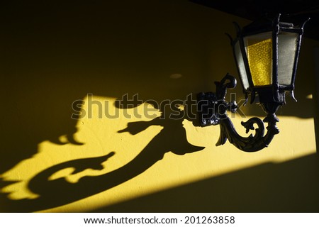 Old fashioned decorative wall lamp casting ornate shadow on bright yellow wall in colonial Brazilian village