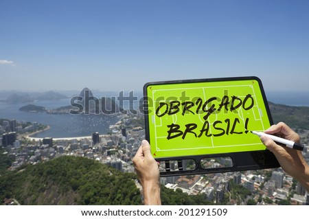 Hands holding Obrigado Brasil Thank You Brazil soccer football tactics board and pen above skyline overlook of Rio de Janeiro