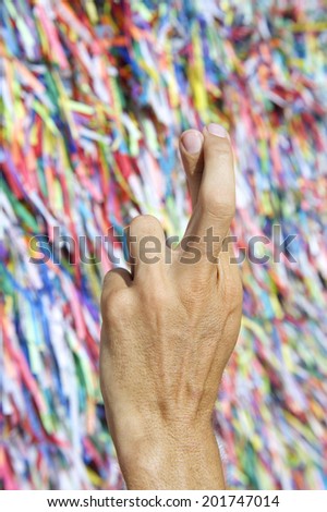 Brazilian hand fingers crossed for luck in front of colorful religious Brazilian wish ribbons fita do Bonfim in Salvador Bahia Brazil