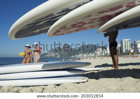 RIO DE JANEIRO, BRAZIL - FEBRUARY 06, 2014: Brazilian women pass stand up paddle rental stand on Ipanema Beach.