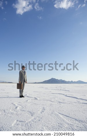 Traveling businessman standing outdoors ready with briefcase looking out on dramatic desert horizon