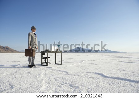 Businessman standing next to mobile office desk outdoors on dramatic white desert landscape