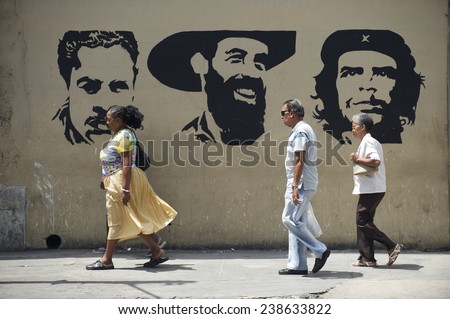 HAVANA, CUBA - MAY, 2011: Cuban people walk in front of stencil billboard featuring Julio Antonio Mella, Camilo Cienfuegos, and Che Guevara, three leaders of the Communist Revolution.