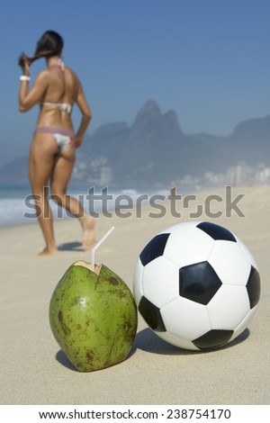 Brazilian woman in bikini walks past fresh green drinking coconut coco gelado and football soccer ball Ipanema Beach Rio de Janeiro Brazil