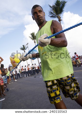 SALVADOR, BRAZIL - FEBRUARY 9, 2013: Brazilian man known as cordeiro holds a crowd control rope alongside a trio electrico music truck on the afternoon Barra Ondina circuit.