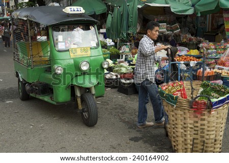 BANGKOK, THAILAND - OCTOBER 27, 2014: Thai market vendor works next to tuk-tuk parked on an alley near the busy flower market.