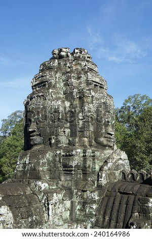 Angkor Wat Temple of Bayon stone face sculptures in front of green trees under blue sky