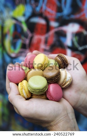 Hands holding pile of colorful French macaroon cookies in front of graffiti background