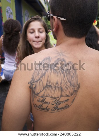 RIO DE JANEIRO, BRAZIL - CIRCA JANUARY, 2013: Young Brazilian man with angel tattoo enjoys a carnival bloco street party with his girlfriend in the Jardim Botanico neighborhood.
