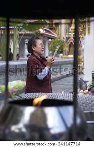 BANGKOK, THAILAND - OCTOBER 26, 2014: Thai woman prays at a Buddhist shrine in front of the Temple of the Emerald Buddha on the grounds of the Grand Palace.