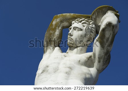 Ancient marble statue of muscular Olympic athlete discus thrower throwing a discus against bright blue sky