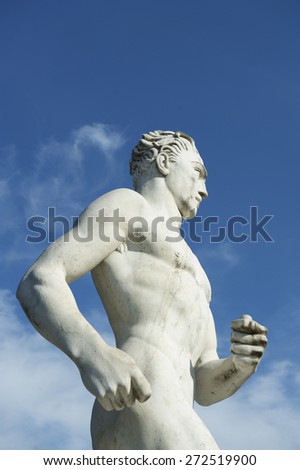 Ancient marble statue of muscular Olympic athlete running against bright blue sky