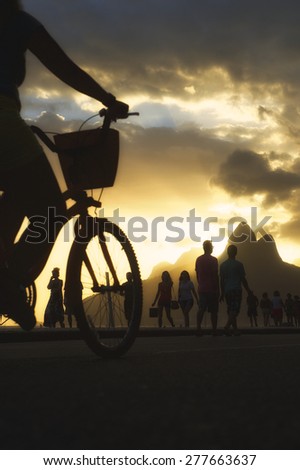 Active silhouettes of people biking and walking on sunset bike path in Ipanema Beach against a backdrop of Two Brothers Mountain Rio de Janeiro Brazil