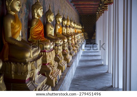 Row of golden seated buddhas in front of decorative wall in a Buddhist temple in Bangkok Thailand