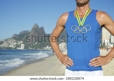 RIO DE JANEIRO, BRAZIL - MARCH 05, 2015: Athlete stands wearing Olympic rings gold medal in front of city skyline view of Ipanema Beach with Two Brothers Mountain.