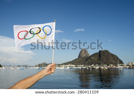 RIO DE JANEIRO, BRAZIL - MARCH 24, 2015: Hand waving Olympic flag on the shore of Botafogo Bay in front of view of Sugarloaf Mountain.