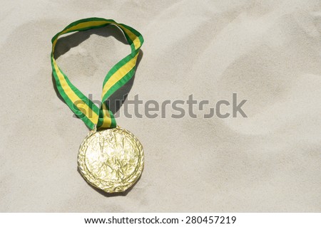Gold medal with Brazilian colors yellow and green ribbon sits in bright sun on the sand of Ipanema Beach Rio de Janeiro Brazil